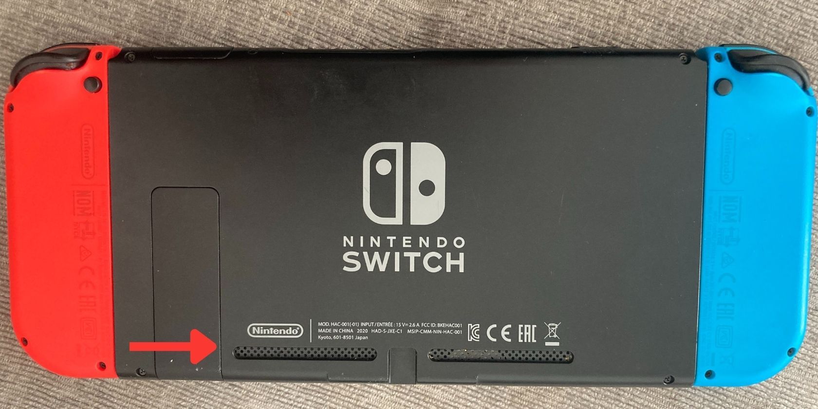 A photograph of a Nintendo Switch on its back with a red arrow pointing towards the air vents