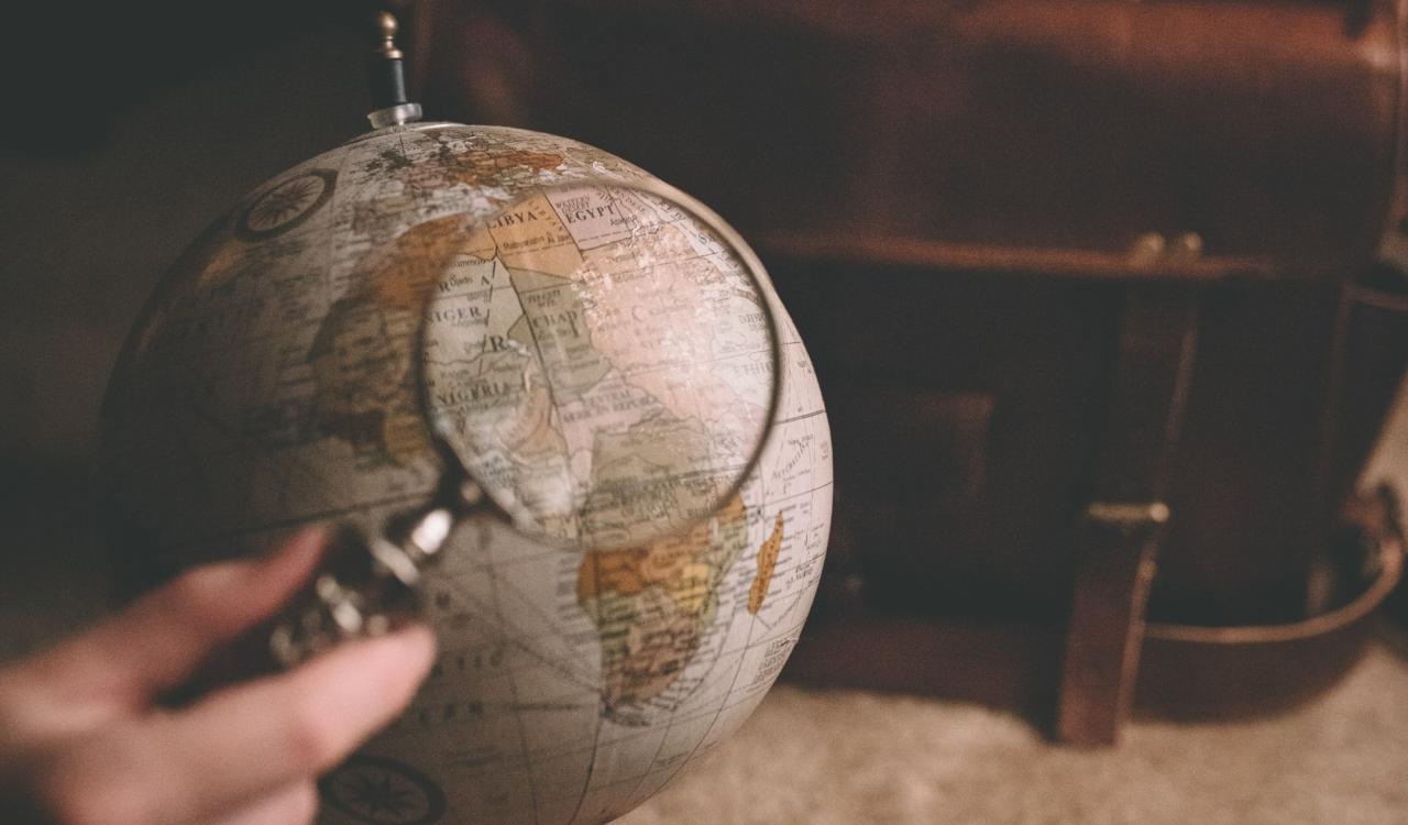 person using magnifying glass on globe figurine