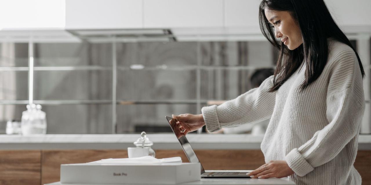 Woman standing and holding MacBook open on a table beside MacBook box