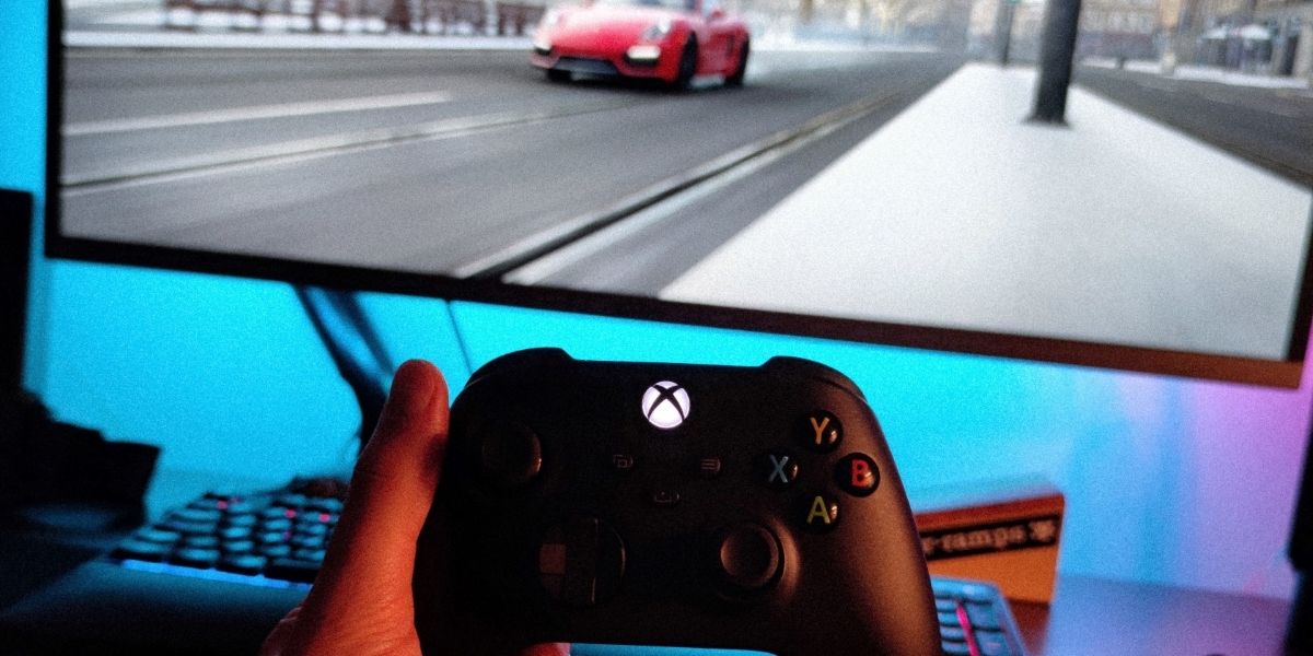 A photo of a standard Xbox Series X Controller being held in front of a monitor 