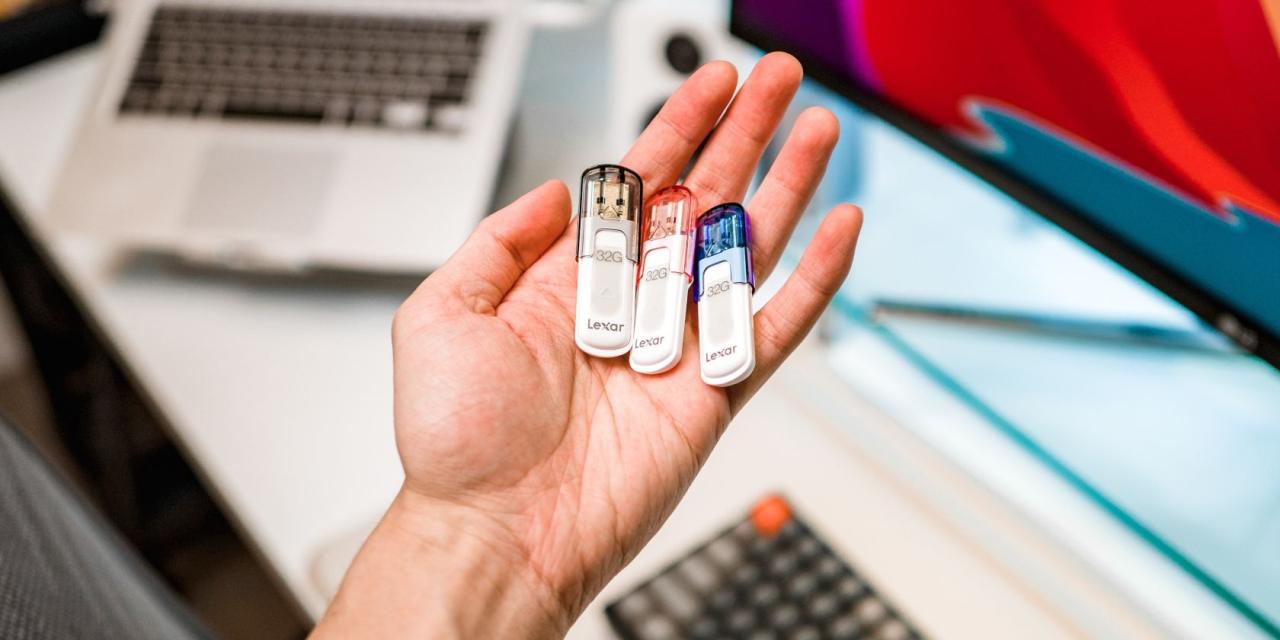 USB drives placed in hand with MacBook and iMac in backgrounds